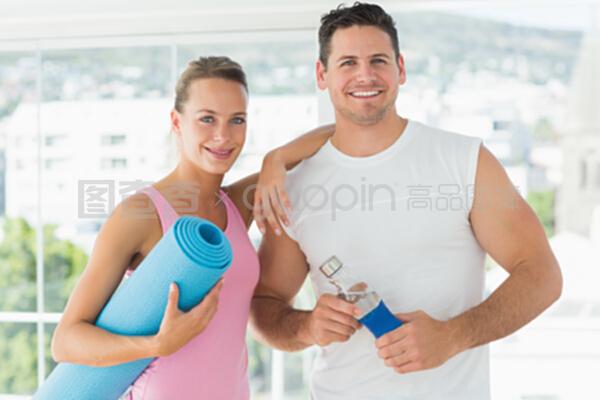 在健身房里,合适的情侣手持水瓶和运动垫